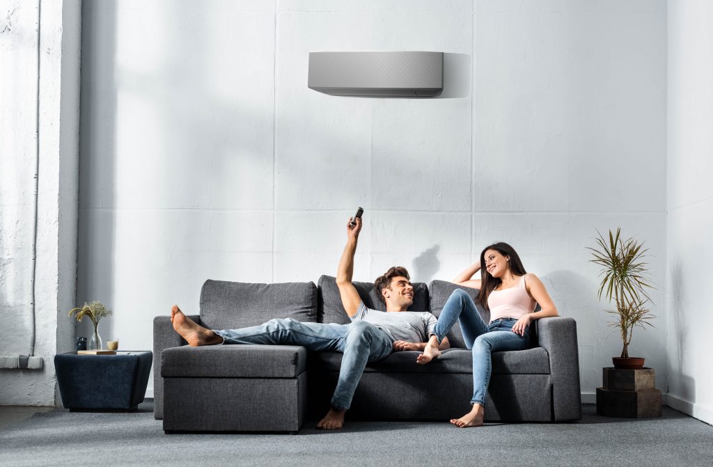 handsome boyfriend switching on air conditioner and looking at smiling girlfriend